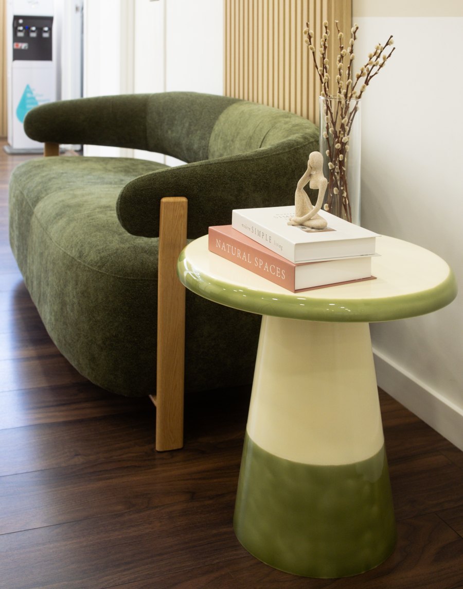 Green velvet sofa and side table with books in the Seena waiting area